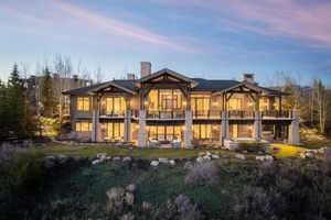 Multi-level property exterior with extensive glass doors, two upper-level balconies, and a lower-level patio featuring a built-in spa