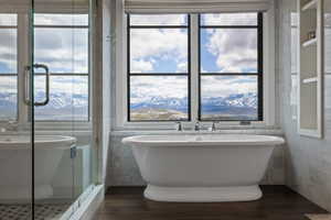 Freestanding soaking tub with a mountain scenery backdrop, set on wood-finish flooring