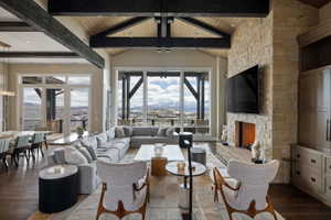 Spacious living area featuring exposed wood beams, vaulted ceilings, a stone-clad fireplace, and expansive windows showcasing distant mountain scenery