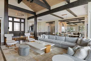 Spacious living area featuring a vaulted wood-paneled ceiling with exposed wood beams, a paneled double-door entry, a large area rug with square patterns, recessed lighting, and multiple distinct lighting fixtures