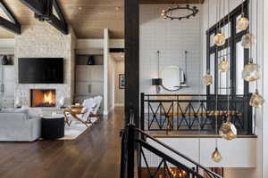 Open-concept living space featuring a stone fireplace with a built-in television, exposed wood ceiling beams, and wood-finish flooring