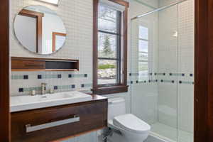 Bathroom featuring a contemporary floating vanity with an integrated rectangular sink, a glass-enclosed shower, a circular mirror, and a window with wood trim