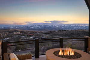 Outdoor terrace featuring a stone fire pit with lava rock, metal railings, and a mountain range backdrop