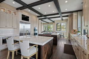 Gourmet kitchen featuring a beamed ceiling, light wood-finish cabinetry, a large island with a countertop, stainless steel appliances, and wood-finish flooring