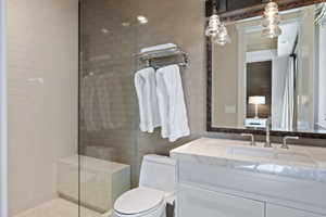 Bathroom featuring a frameless glass shower enclosure with subway tile surround, white vanity with stone countertop, integrated sink, and dual handle faucet