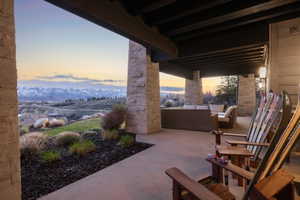 Covered patio featuring stone pillars, exposed beam ceiling, concrete flooring, and surrounding landscape