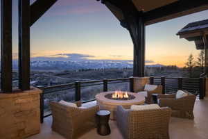 Covered outdoor patio featuring a built-in fire pit, stone-clad pillars, and a metal railing system