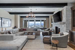 Spacious living area featuring exposed ceiling beams, a stone-clad fireplace, large windows, a prominent chandelier, and built-in cabinetry