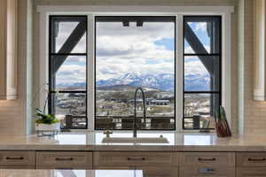 Kitchen sink with a gooseneck faucet, set within a light-toned countertop, framed by large windows featuring black mullions and trim
