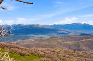 Expansive mountainous landscape featuring rolling hills and distant snow-capped peaks under a blue sky with scattered clouds