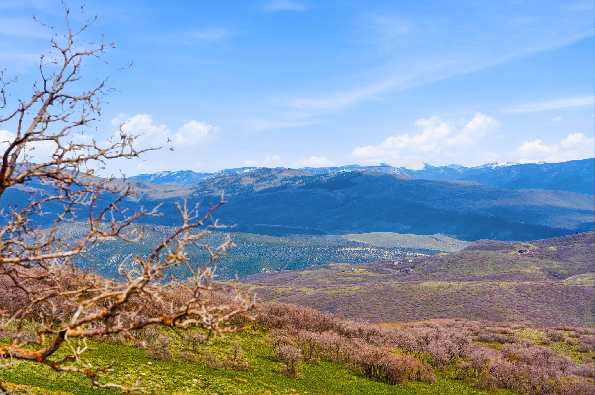 Expansive mountain landscape featuring distant snow-capped peaks under a blue sky with scattered clouds