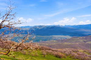 Expansive mountain landscape featuring distant snow-capped peaks under a blue sky with scattered clouds