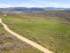 Expansive rural landscape featuring a winding unpaved road, varied green terrain, and distant mountains under a blue sky