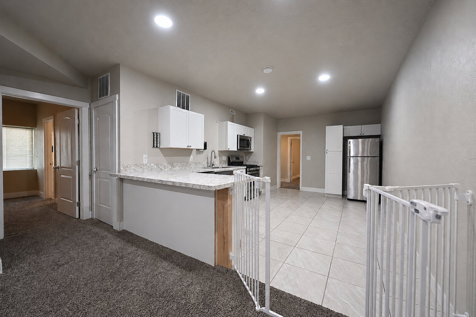 Open-concept kitchen and living area featuring white cabinetry, stainless steel appliances, speckled countertops, and recessed lighting