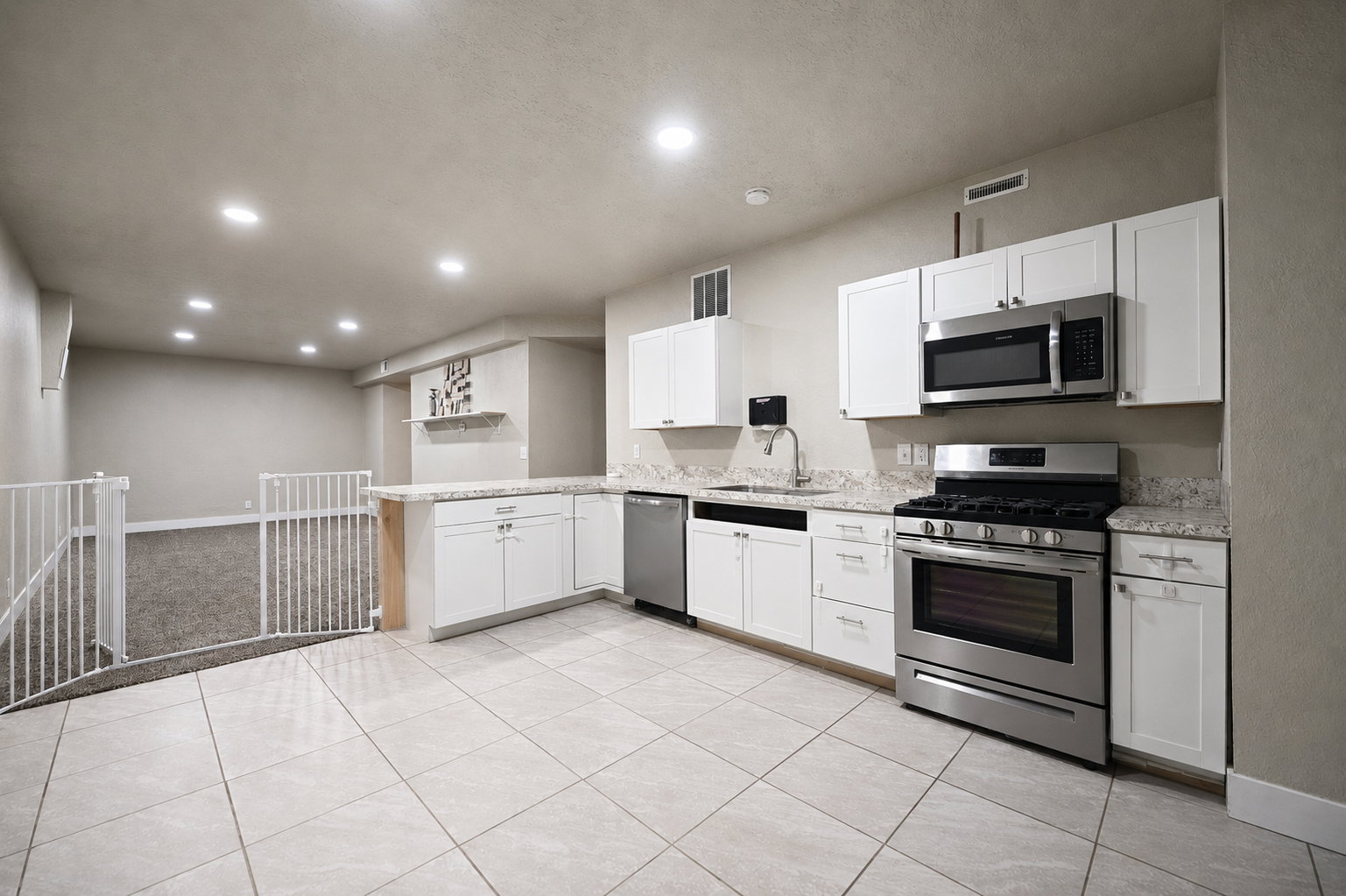 Kitchenette featuring white cabinetry, granite-style countertops, stainless steel appliances, and large format tile flooring