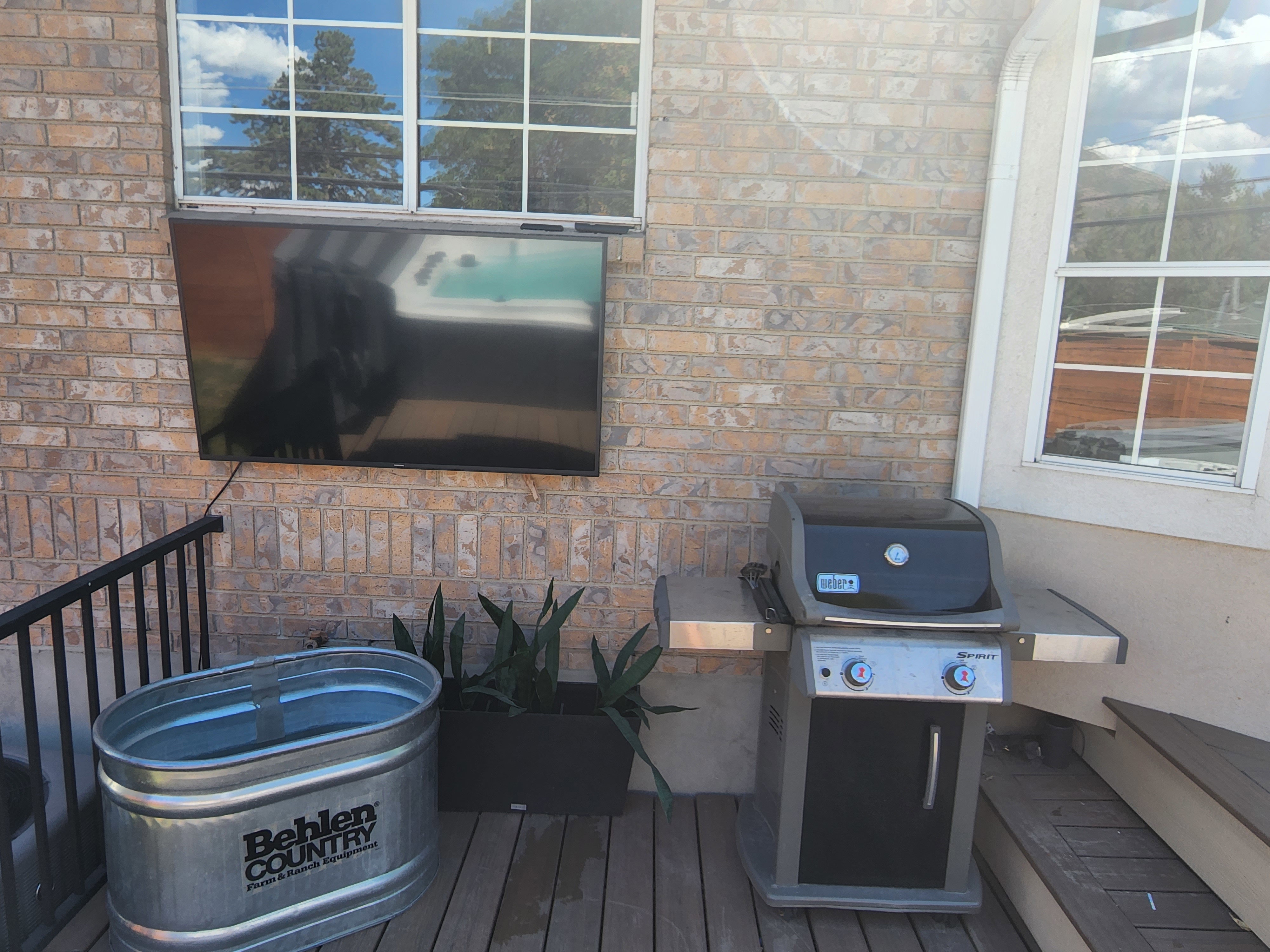 Outdoor entertainment area featuring a mounted television, brick exterior, and wood-finish decking