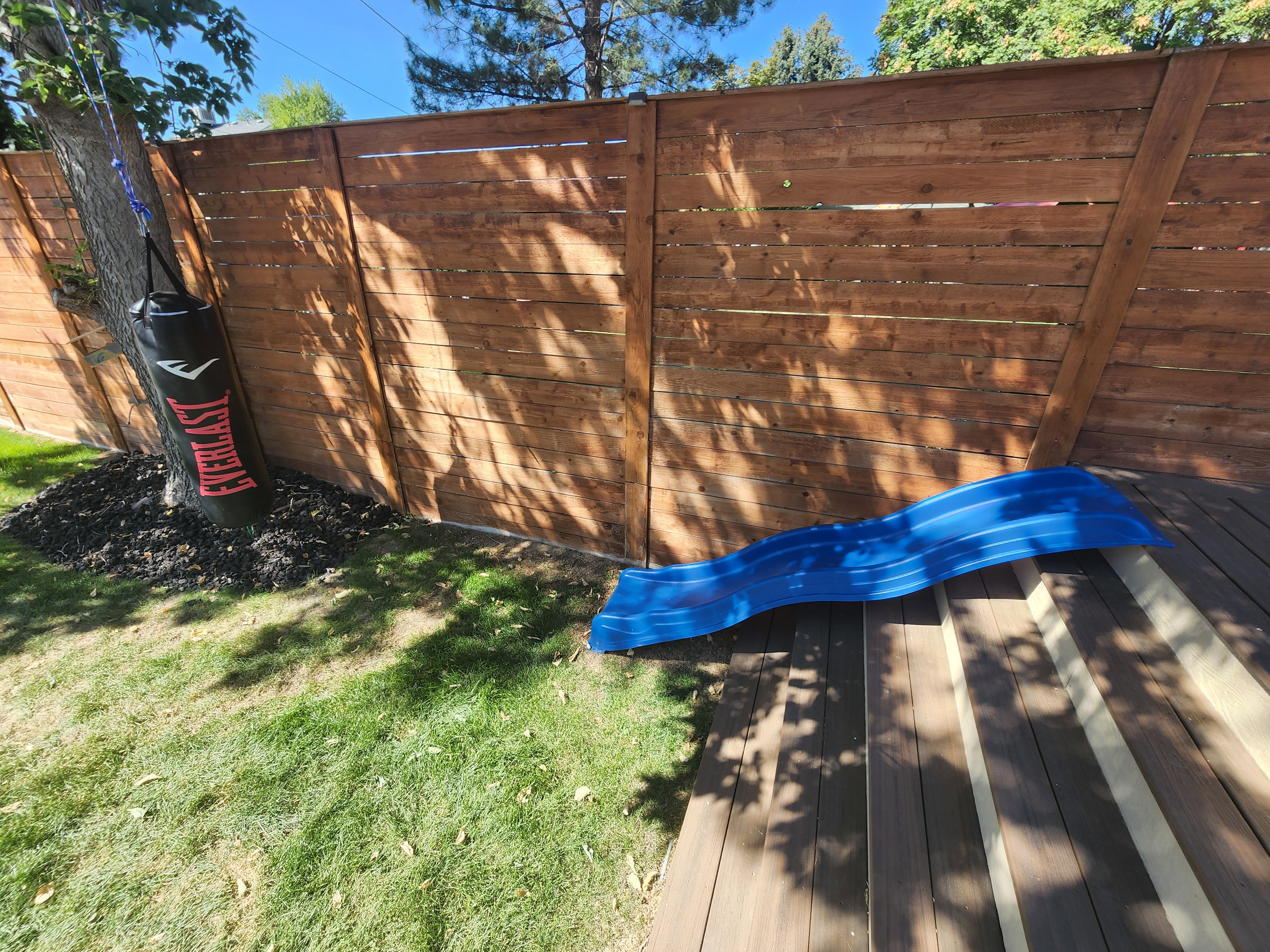 Expansive wood deck with stairs leading to a grassy yard, featuring a privacy fence and mature trees