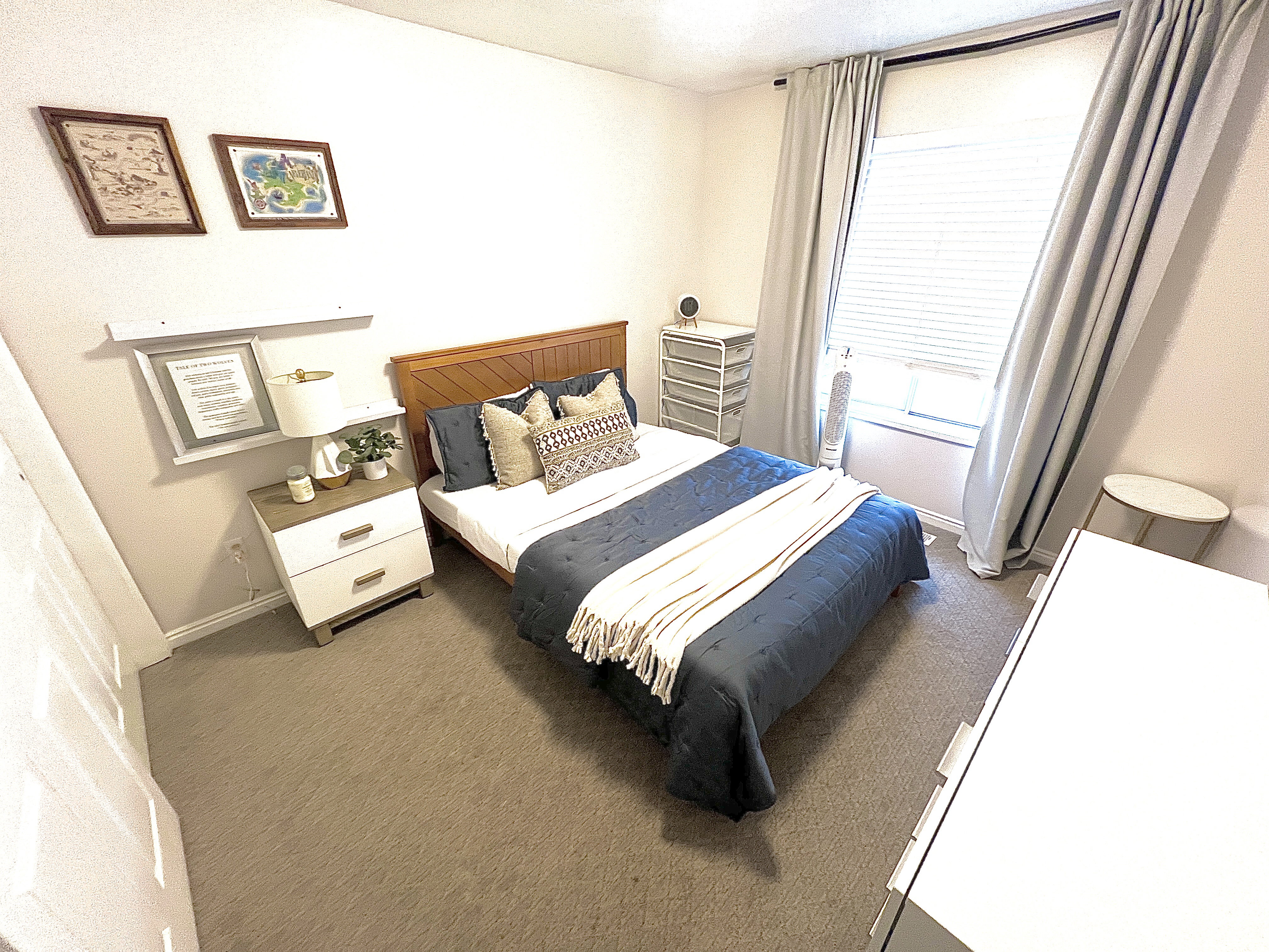 Bedroom featuring a wood-finish headboard, window with blinds and drapes, and a built-in floating shelf