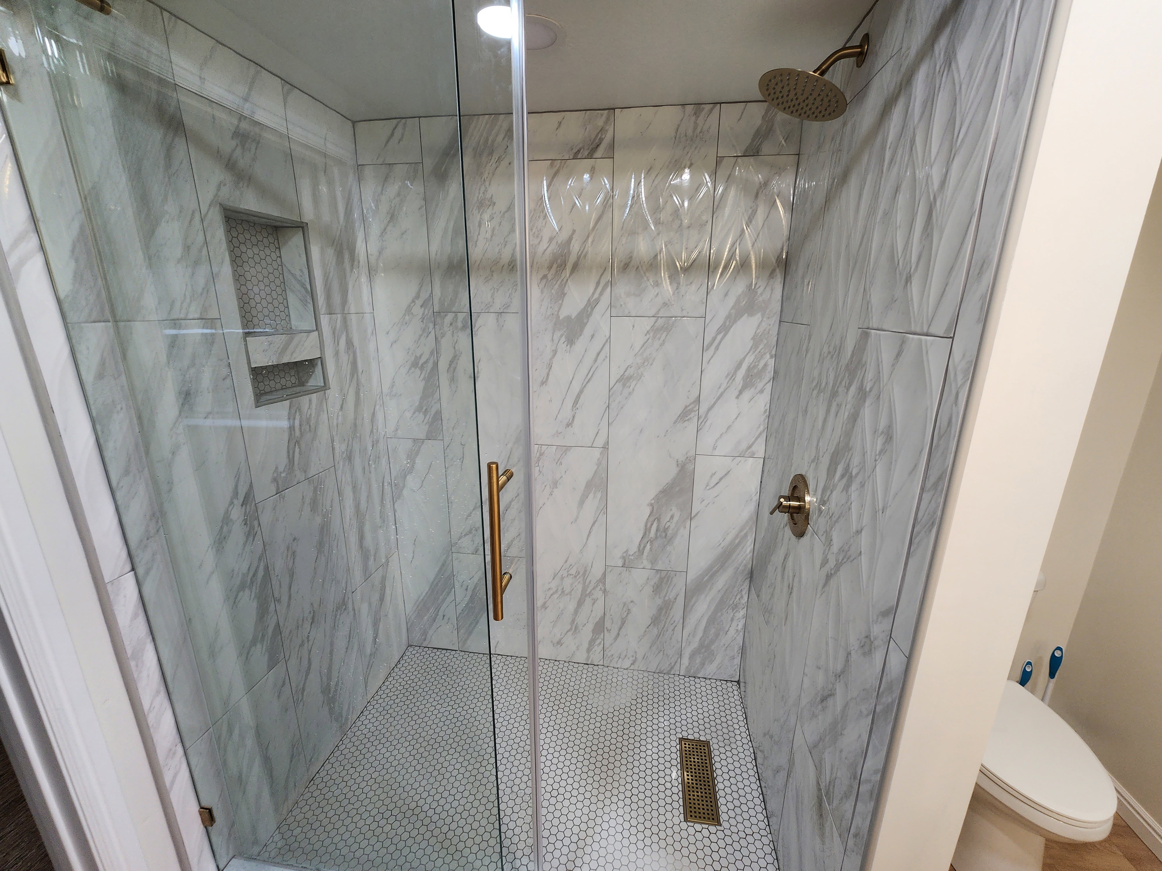 Glass-enclosed shower with large-format tile walls, recessed niche shelving, and a mosaic tile floor