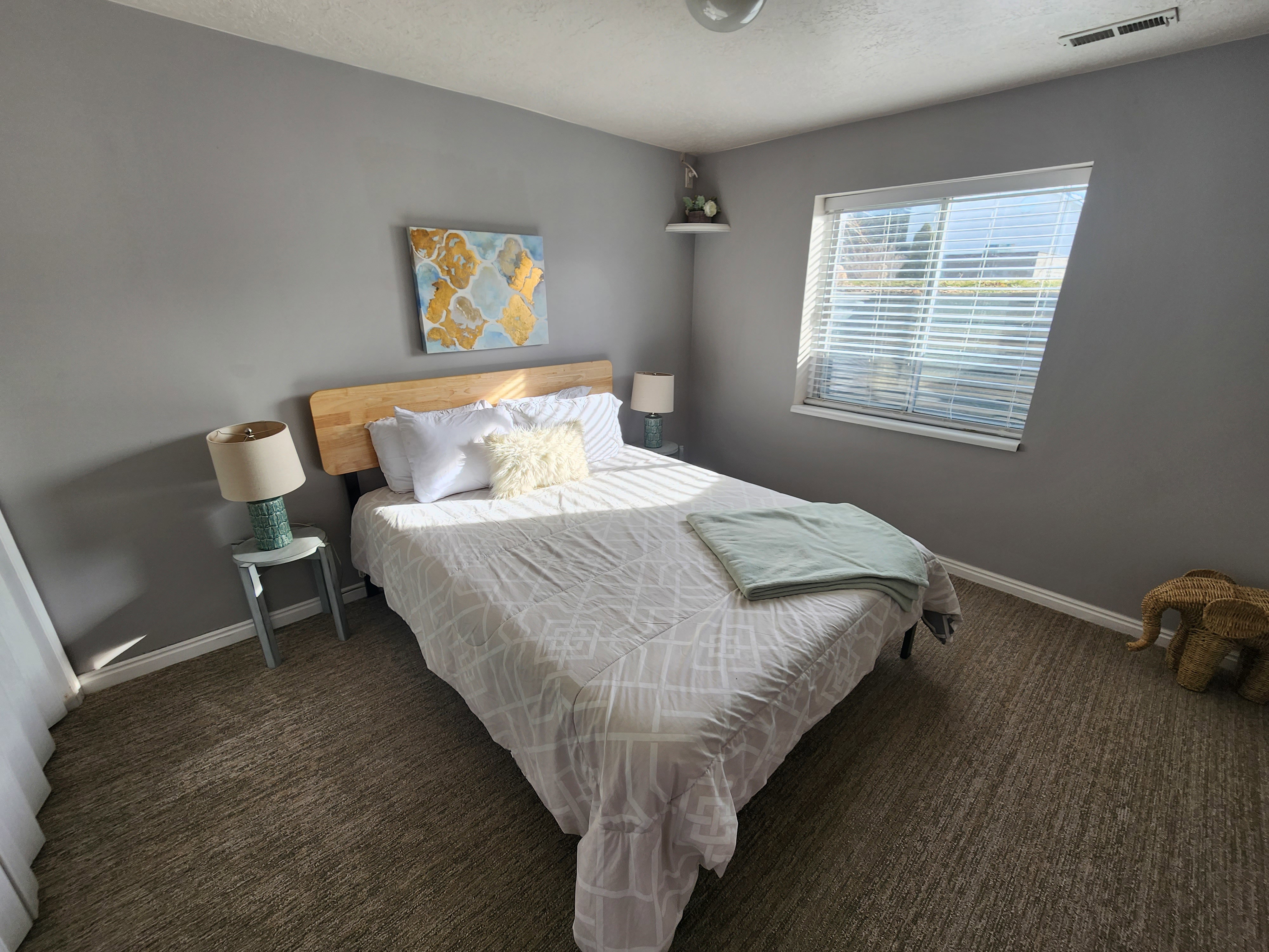Bedroom featuring neutral gray walls, a large window with blinds, and textured carpeting