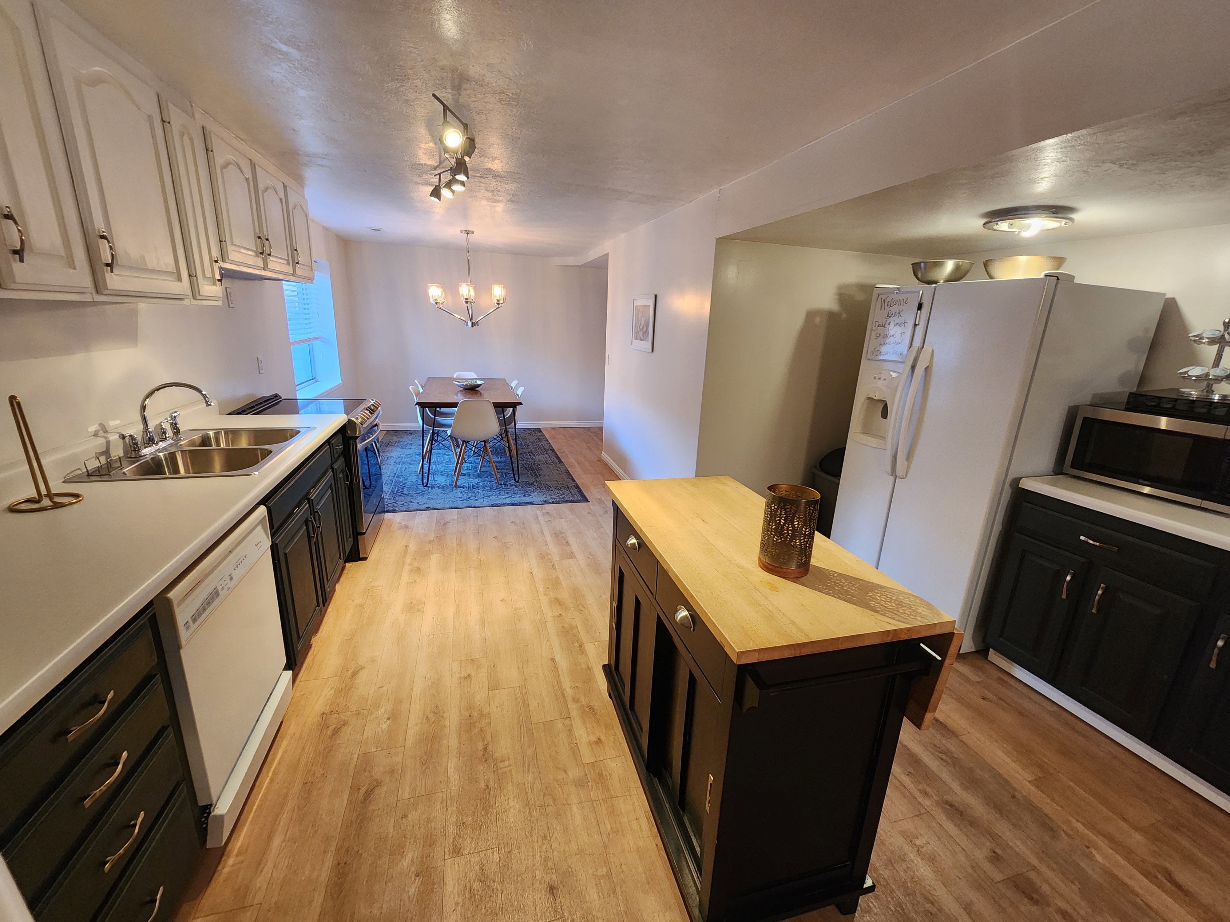 Kitchen featuring wood-finish flooring, two-tone cabinetry with white upper and dark lower cabinets, and a double basin stainless steel sink