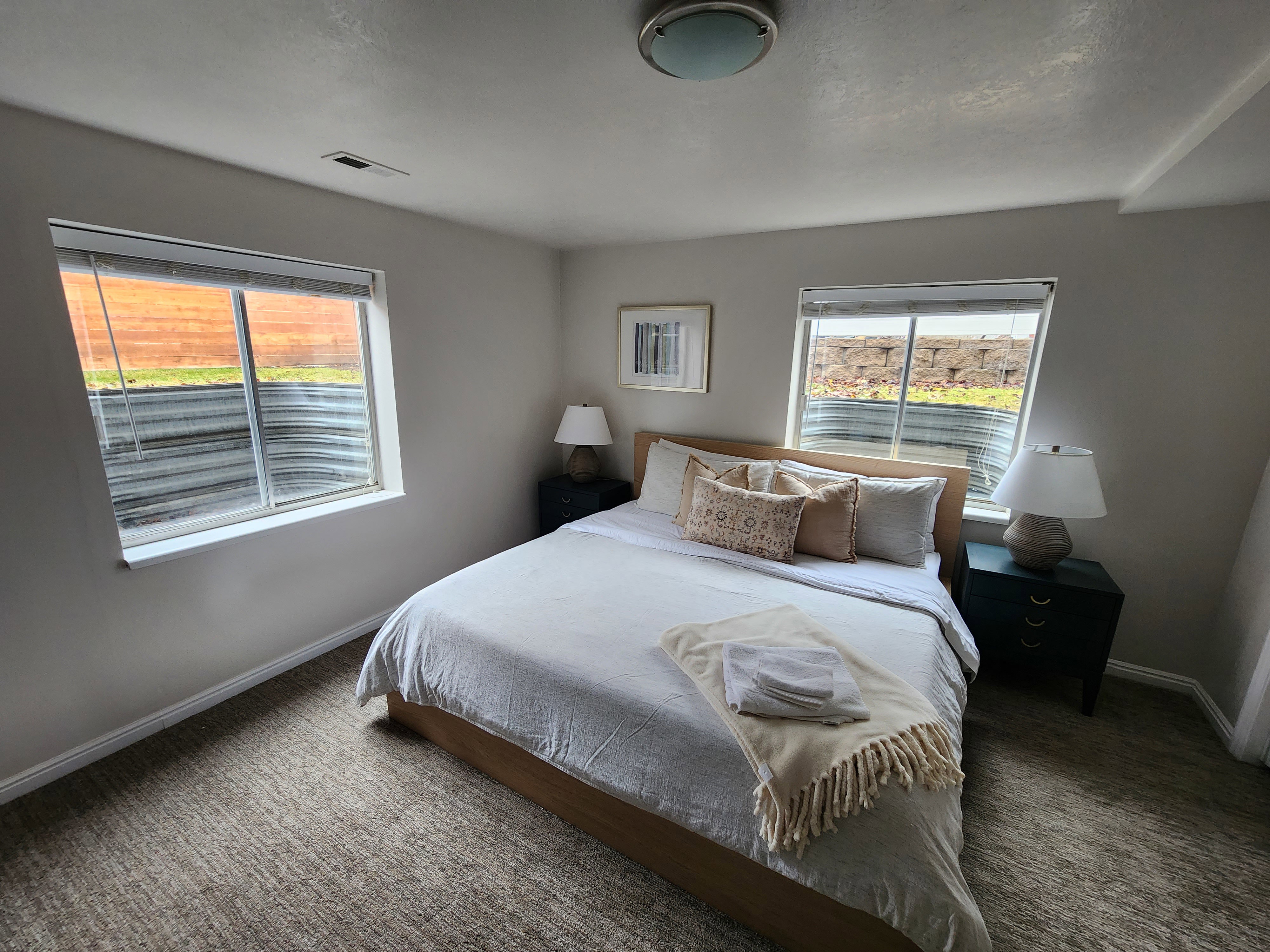 Bedroom featuring two egress windows with window wells, textured carpet flooring, and a flush-mount ceiling light fixture