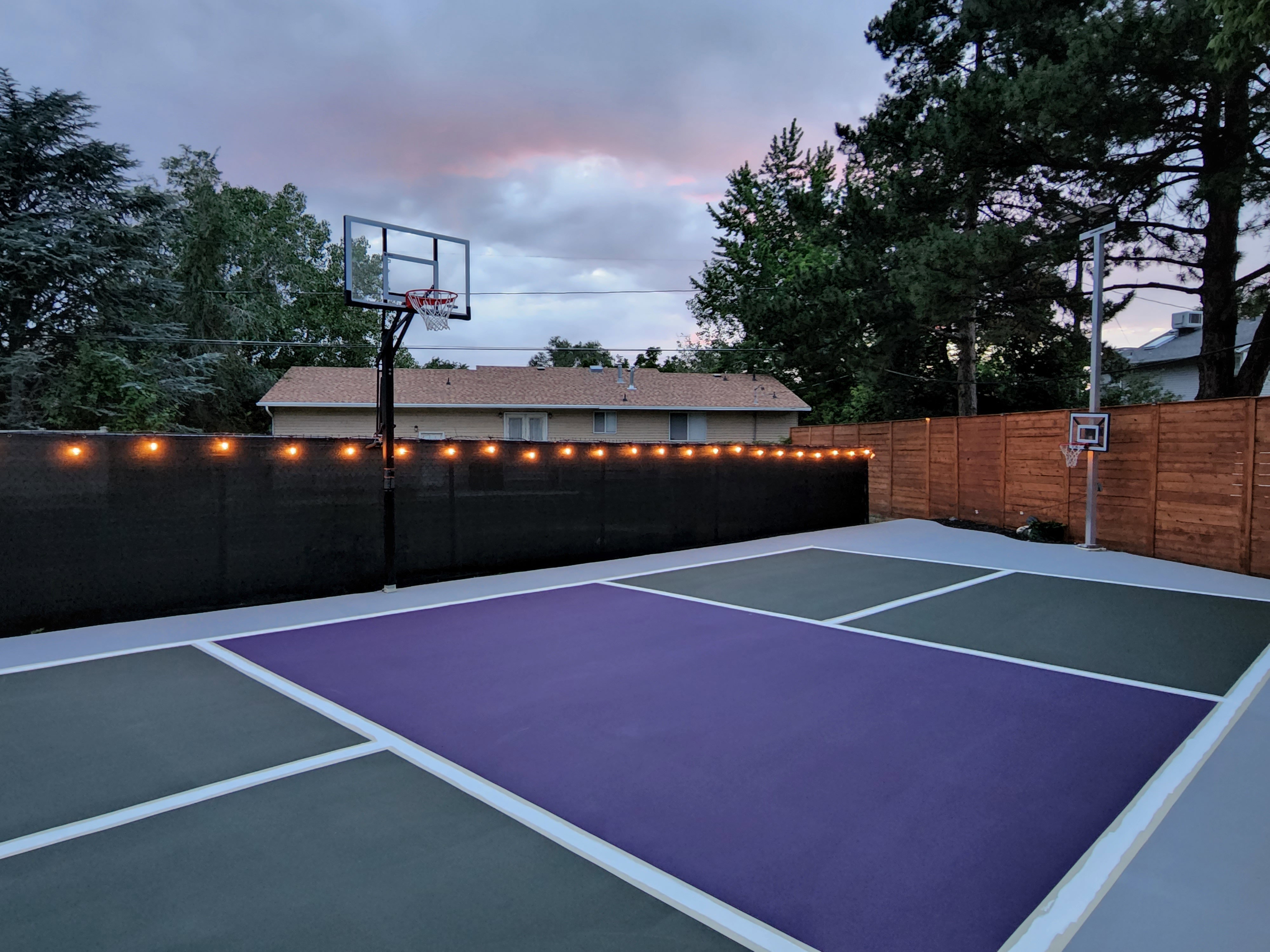 Multi-sport court featuring purple, gray, and white surface markings, two basketball hoops, and perimeter lighting