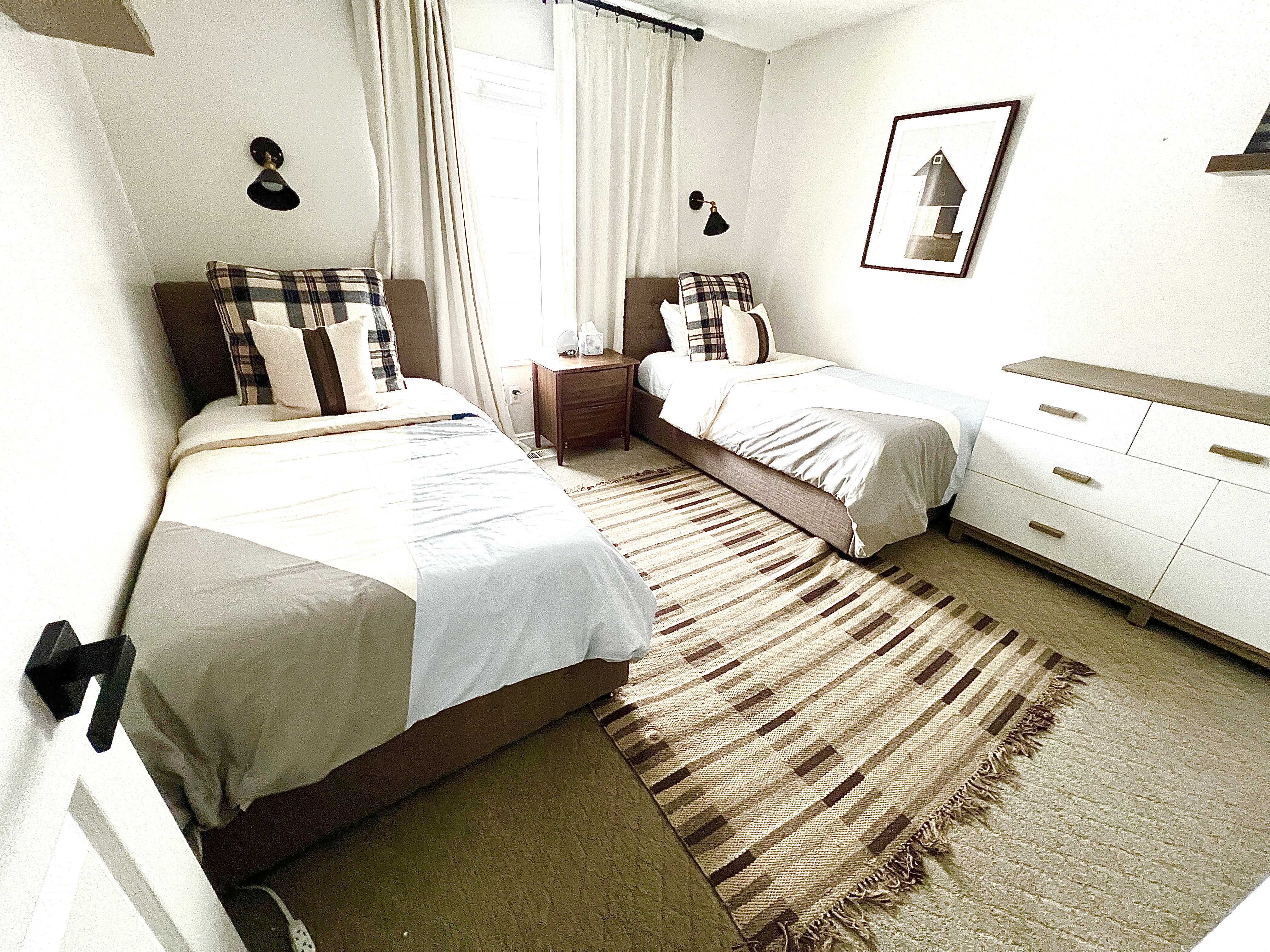 Room featuring two beds with upholstered headboards, sconce lighting, and carpeted flooring