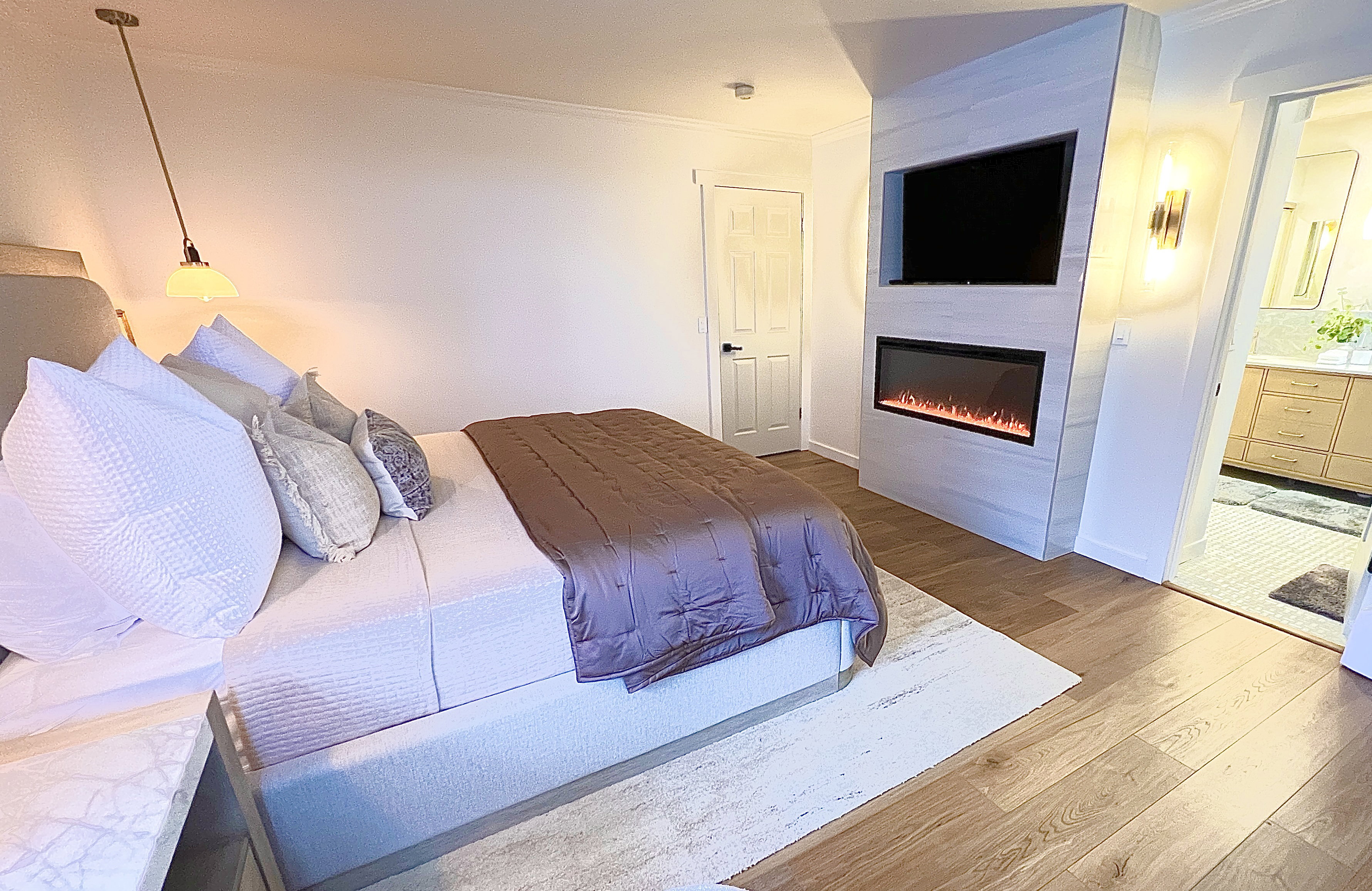 Bedroom featuring wood-finish flooring, a built-in electric fireplace, recessed television niche, and a wall-mounted sconce