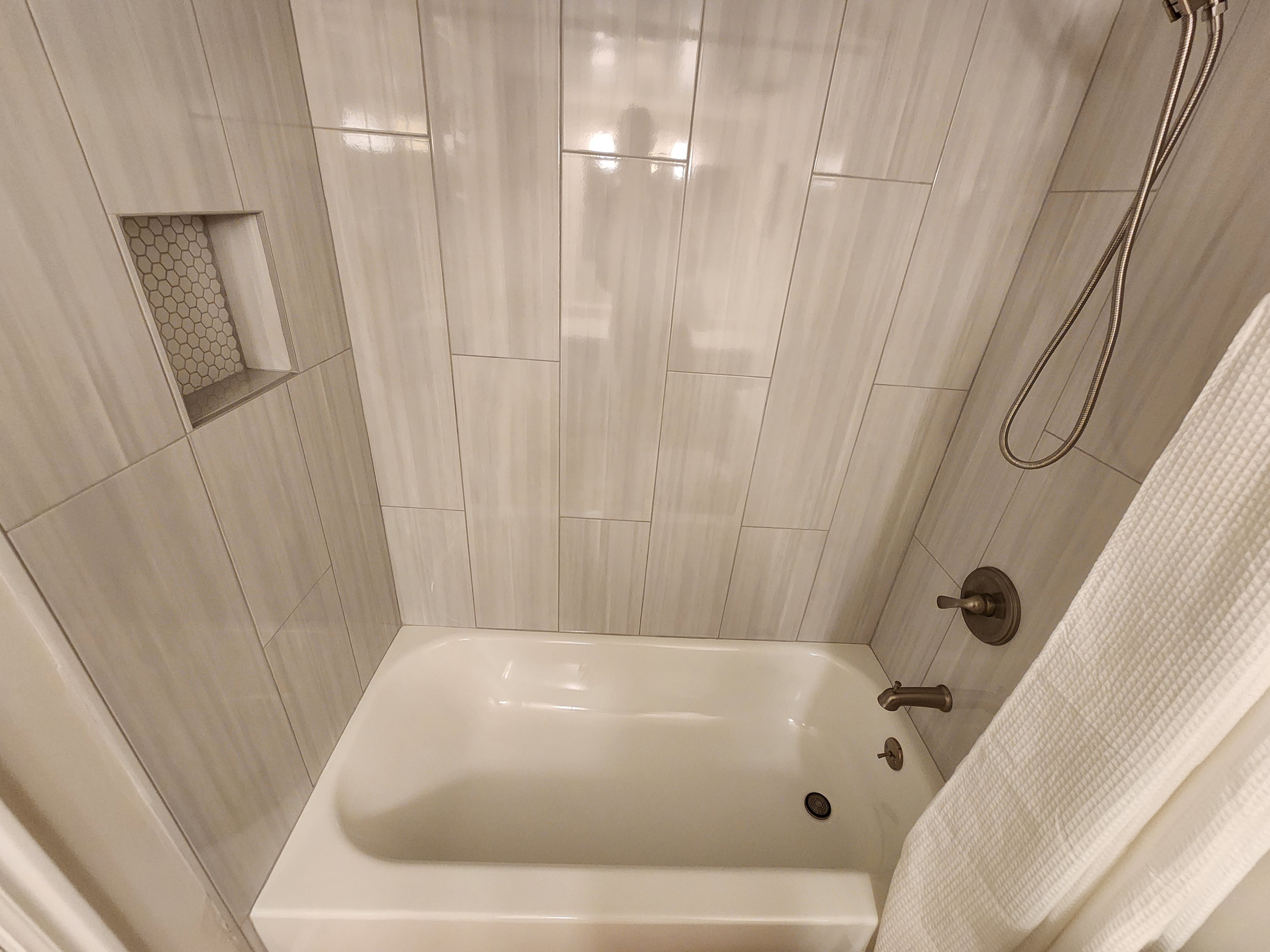 Bathtub and shower combination featuring floor-to-ceiling tile surround, a built-in shower niche with mosaic tile, and a handheld showerhead