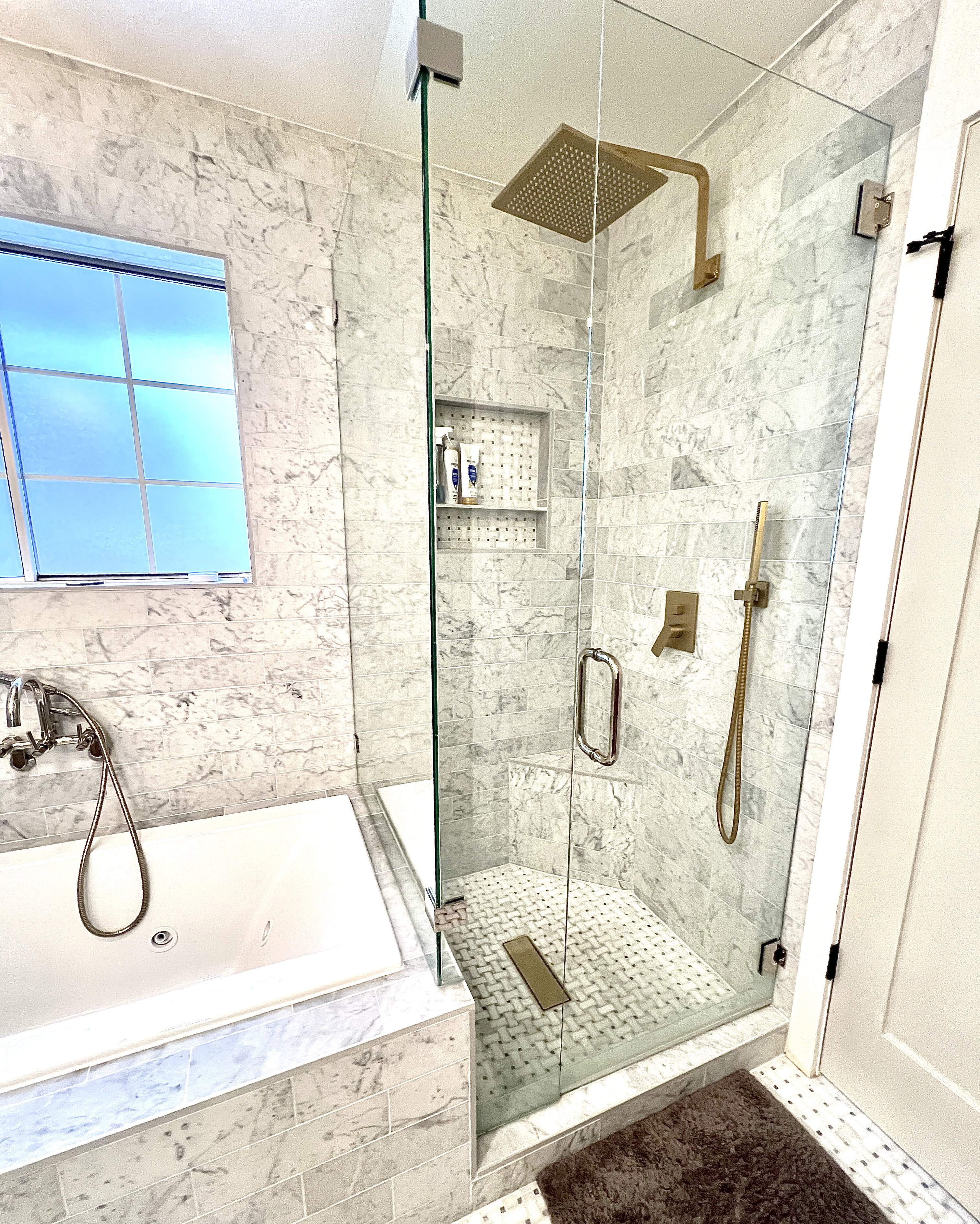 Glass-enclosed shower with gold-tone fixtures, rain shower head, and built-in tiled niche