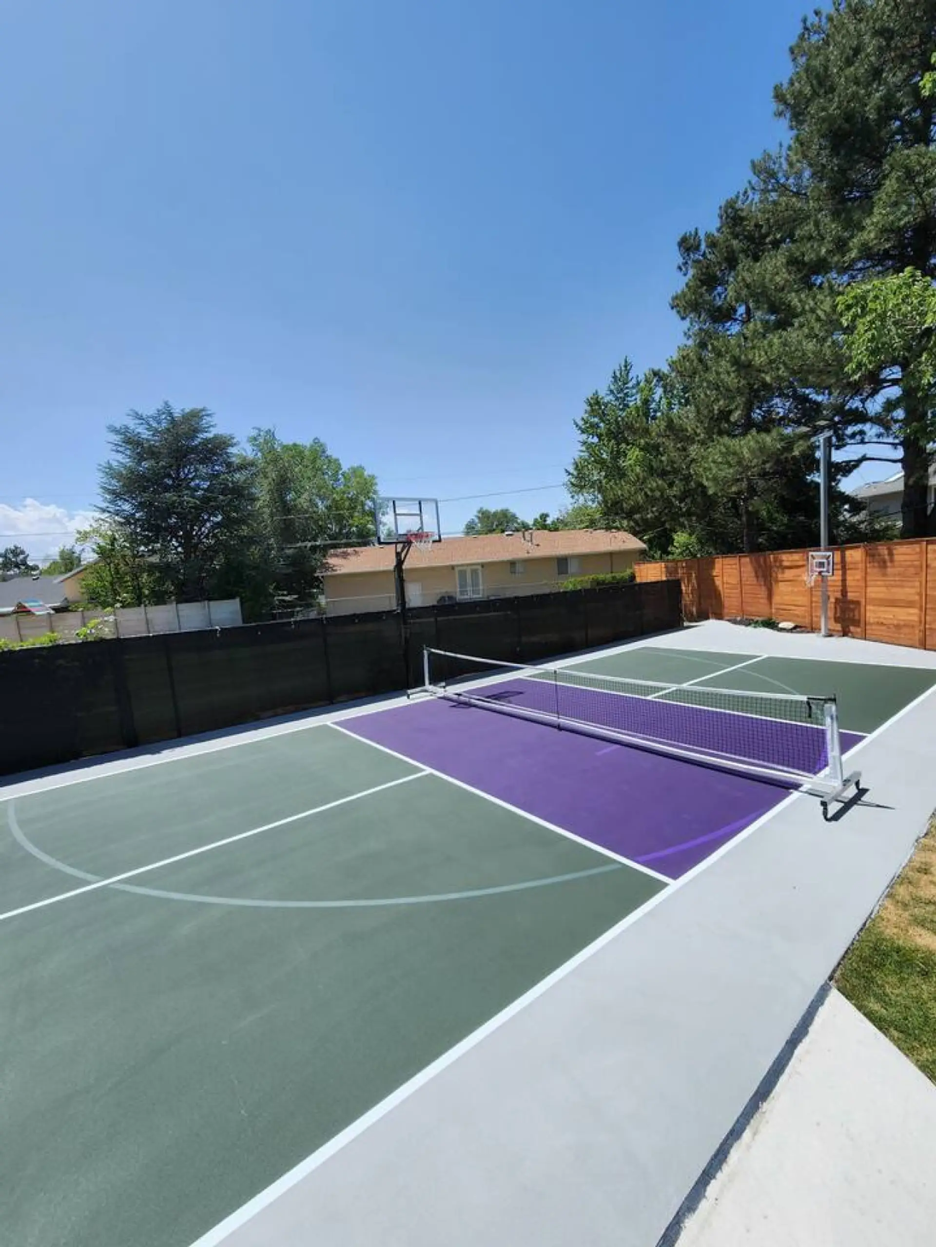 Multi-sport court featuring pickleball and basketball lines, a portable net, and a surrounding privacy fence