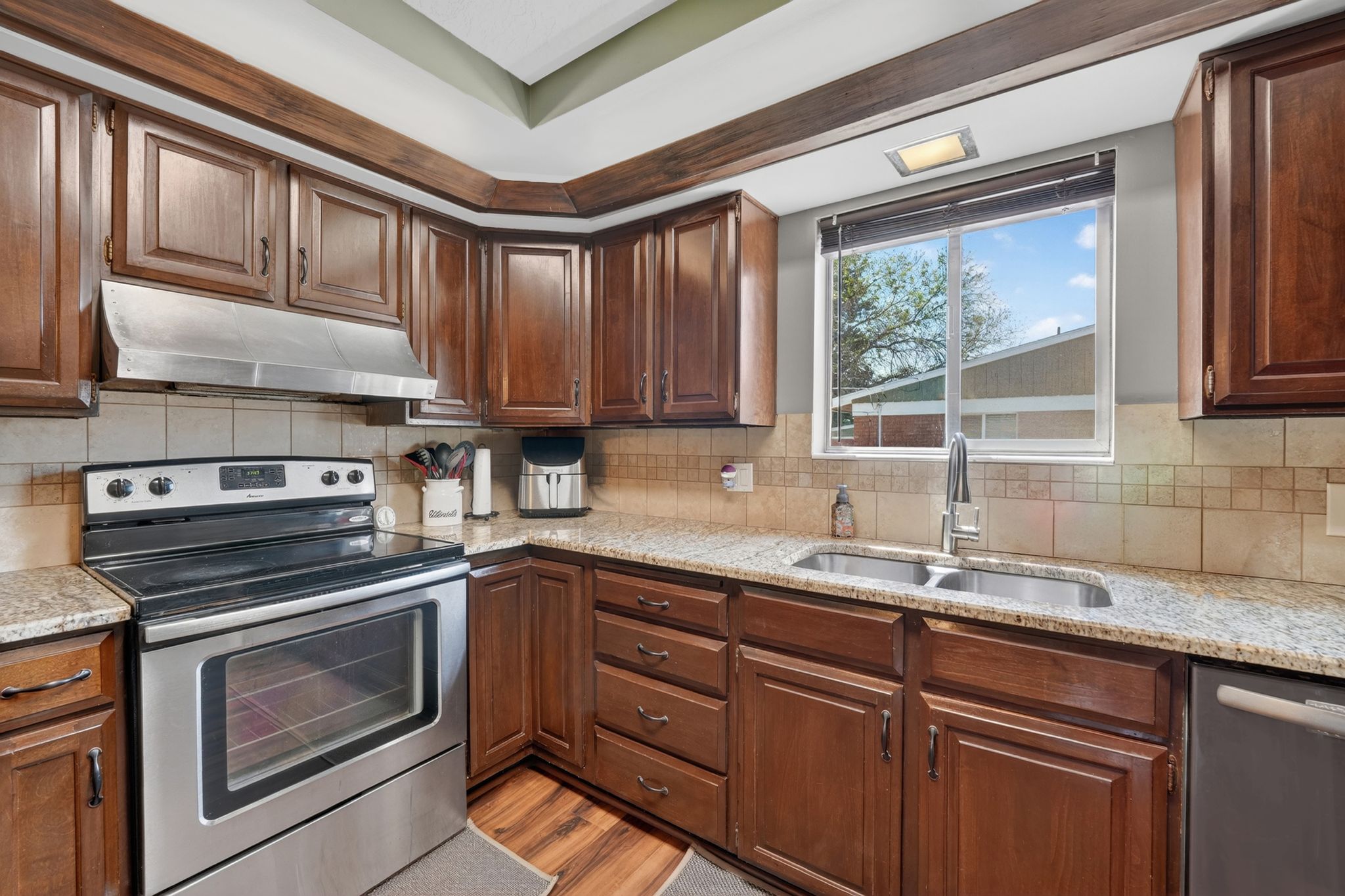 Kitchen featuring wood cabinetry, light-toned countertops, a stainless steel range with overhead vent, and a double basin sink beneath a window
