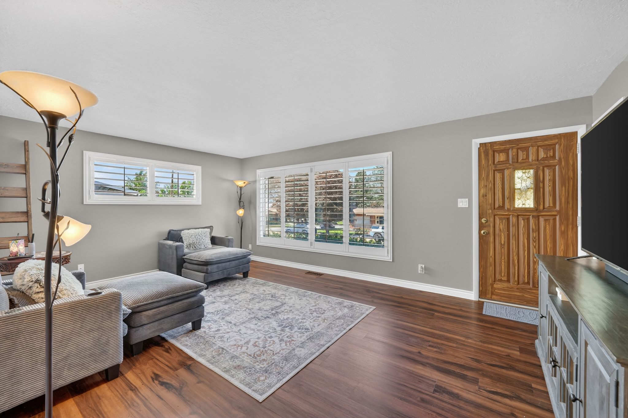 Living area featuring wood-finish flooring, a paneled wood entry door, and multiple windows with plantation shutters