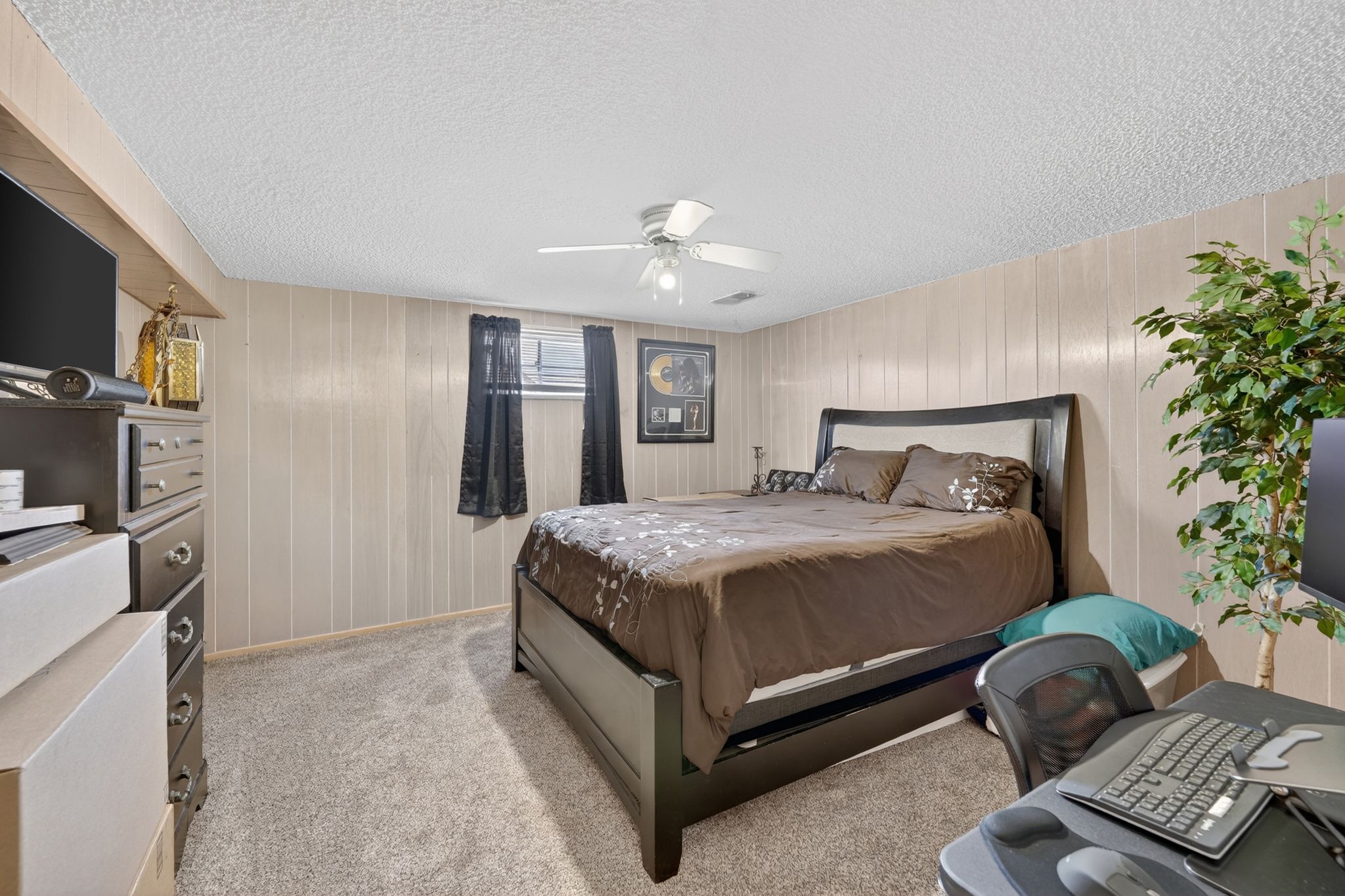 Carpeted room with vertical wall paneling, two windows with dark coverings, and a ceiling fan with light fixture