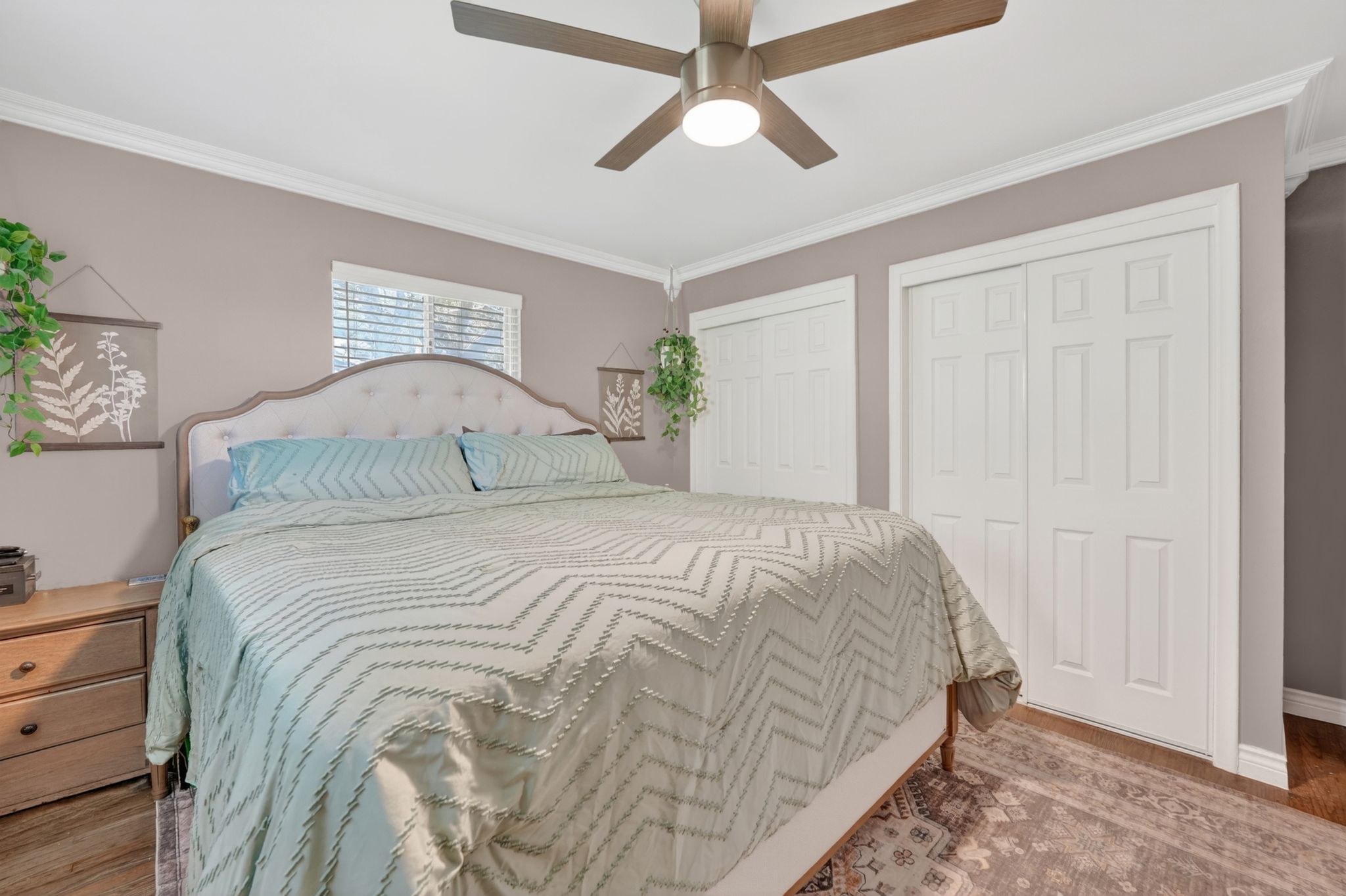 Bedroom featuring a ceiling fan, crown molding, a window with blinds, and two sets of bi-fold closet doors