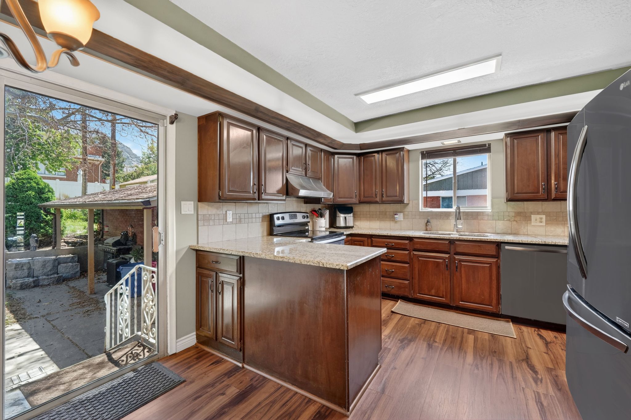 Kitchen featuring wood-finish flooring, dark wood cabinetry, light-toned granite countertops, and a tile backsplash