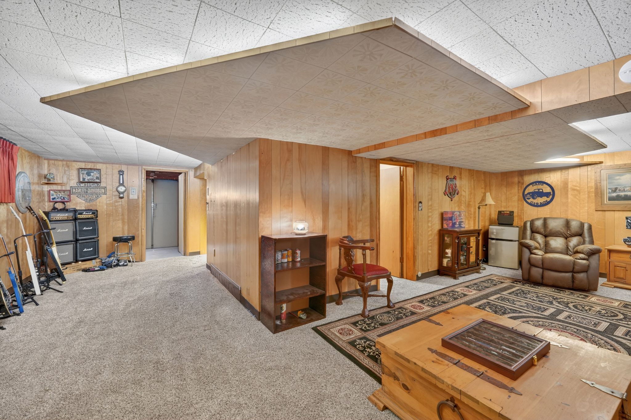 Finished lower level featuring light wood-finish paneling, drop ceiling, and neutral carpet flooring