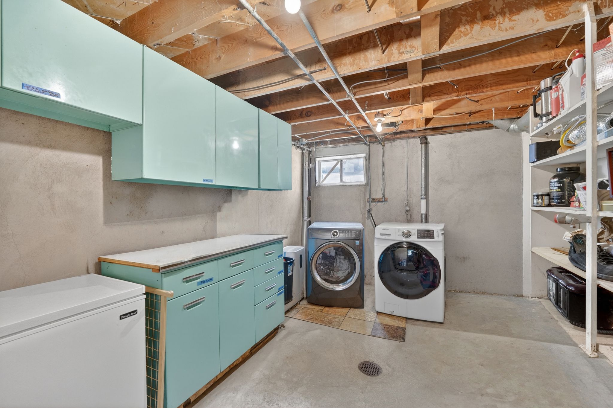 Laundry area featuring exposed ceiling beams, a window, and concrete flooring