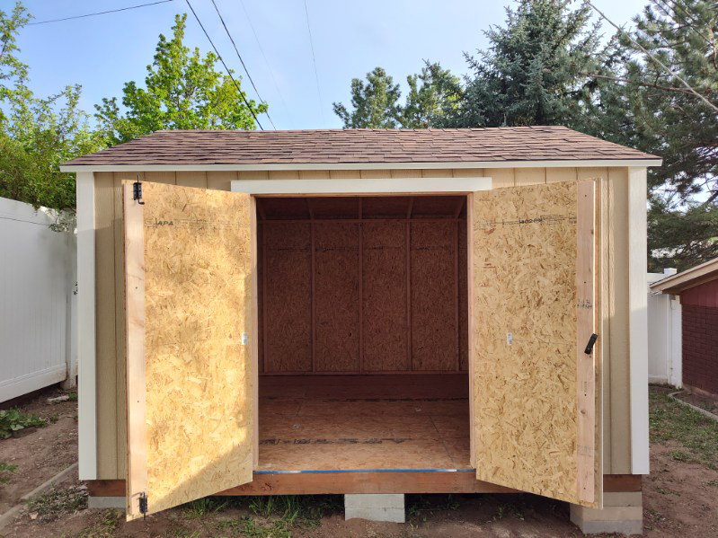 Newly constructed shed featuring a shingled roof, neutral-toned siding, and double doors