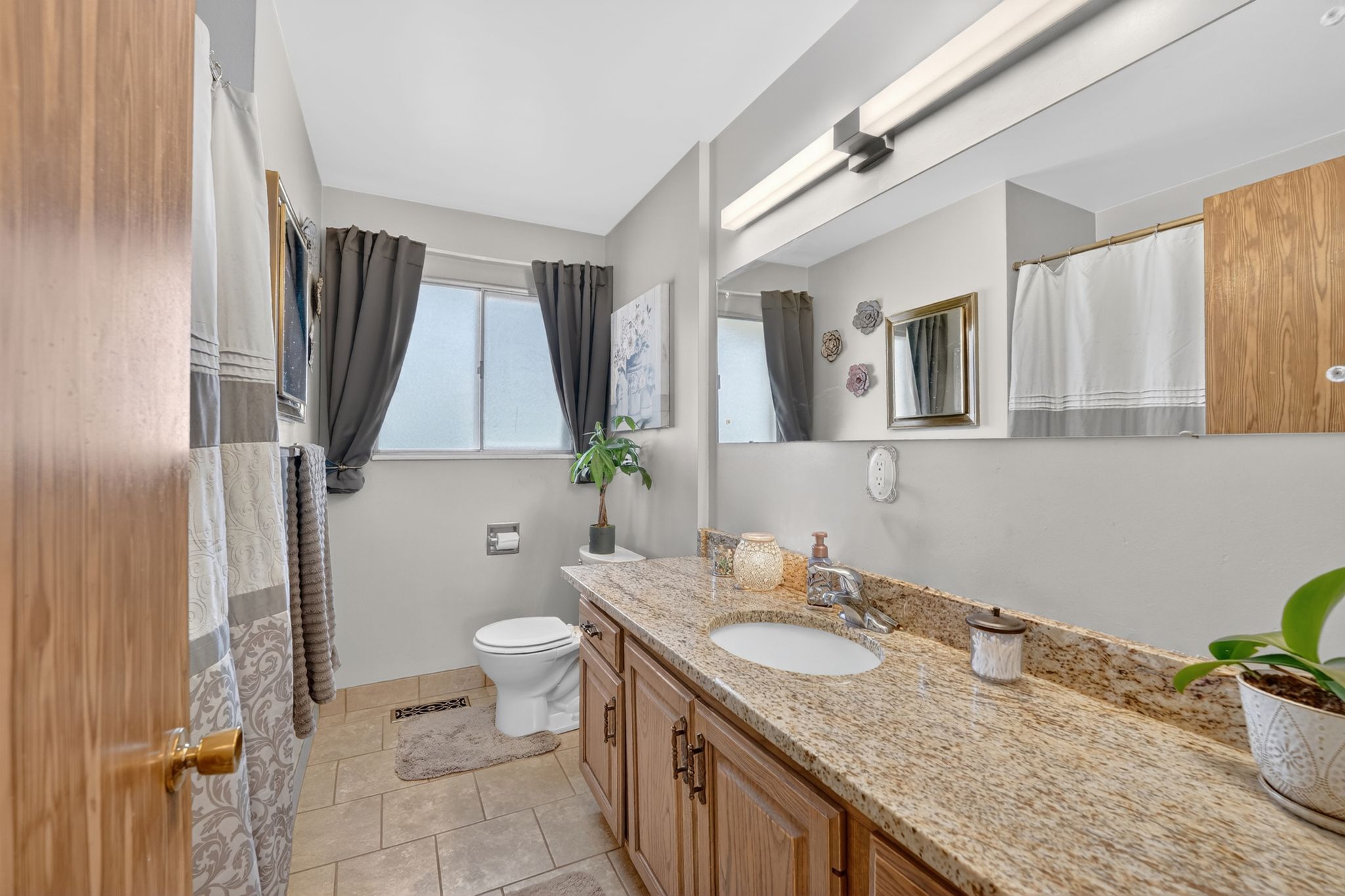 Bathroom featuring a wood-finish vanity with a granite-style countertop, undermount sink, and a large wall-mounted mirror