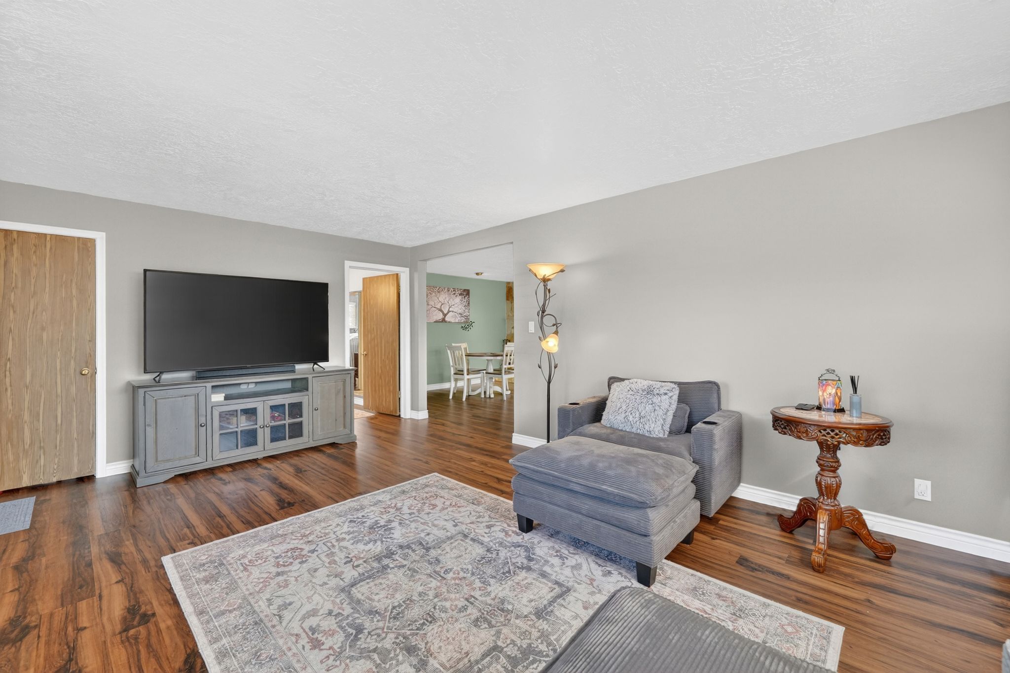 Spacious living area featuring wood-finish flooring, light gray wall paint, white baseboards, and a wide entryway