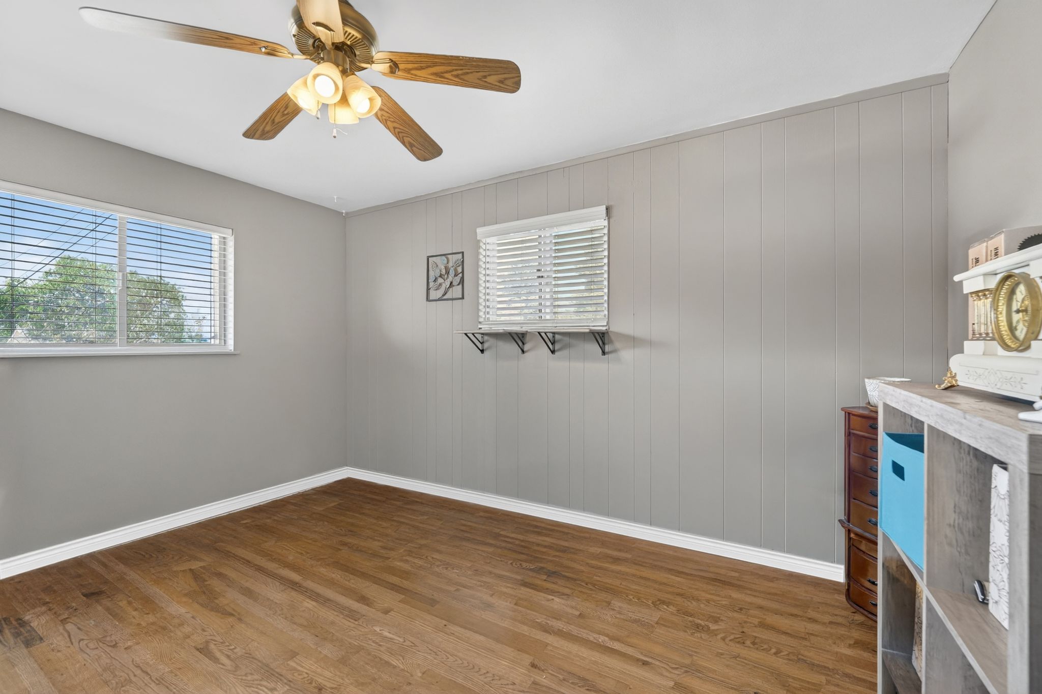 Room featuring wood-finish flooring, a ceiling fan with integrated lighting, and a window with horizontal blinds
