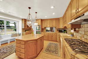 Kitchen featuring wood-finish cabinetry, an octagonal island with storage, tile countertops, and a gas range