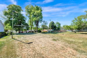 Backyard featuring a volleyball net, mature trees, and open lawn space