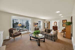 Spacious living area featuring carpet flooring, recessed ceiling lighting, and large windows with integrated plantation shutters