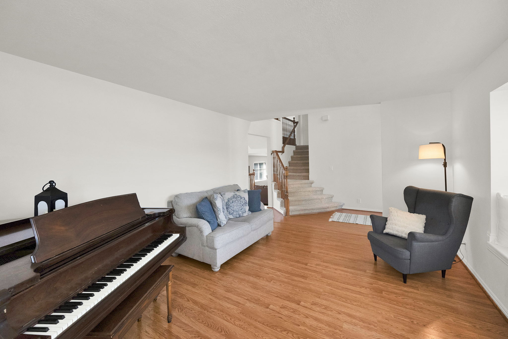 Spacious living area featuring wood-finish flooring, light-toned walls, and a staircase with wood railing and carpeted treads