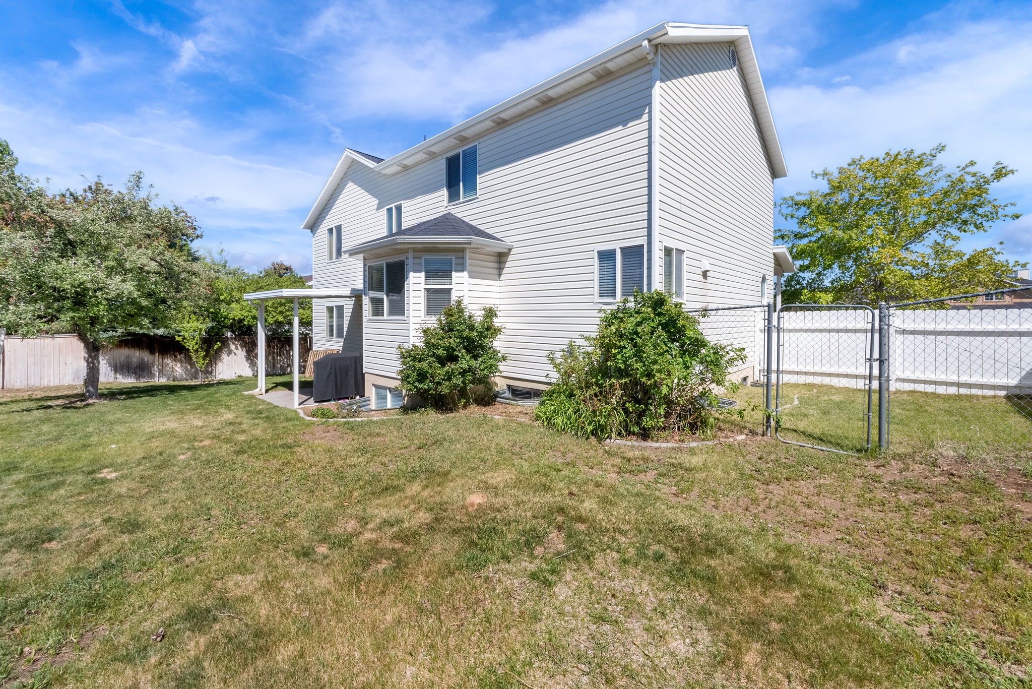 Spacious backyard with a paved patio, covered pergola, and mature trees