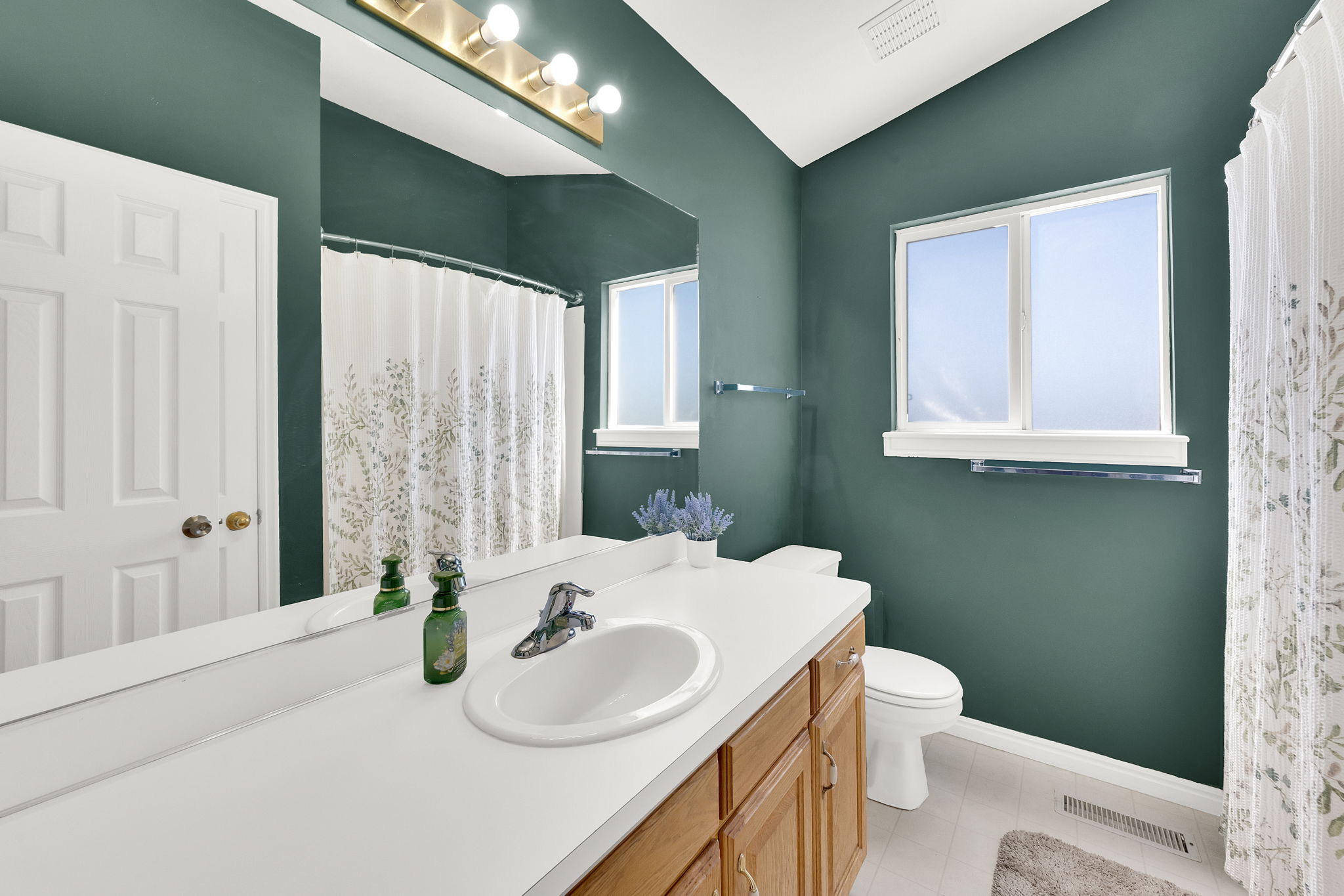 Bathroom featuring a single vanity with wood cabinetry and an integrated sink, a large mirror, a window, and a vaulted ceiling