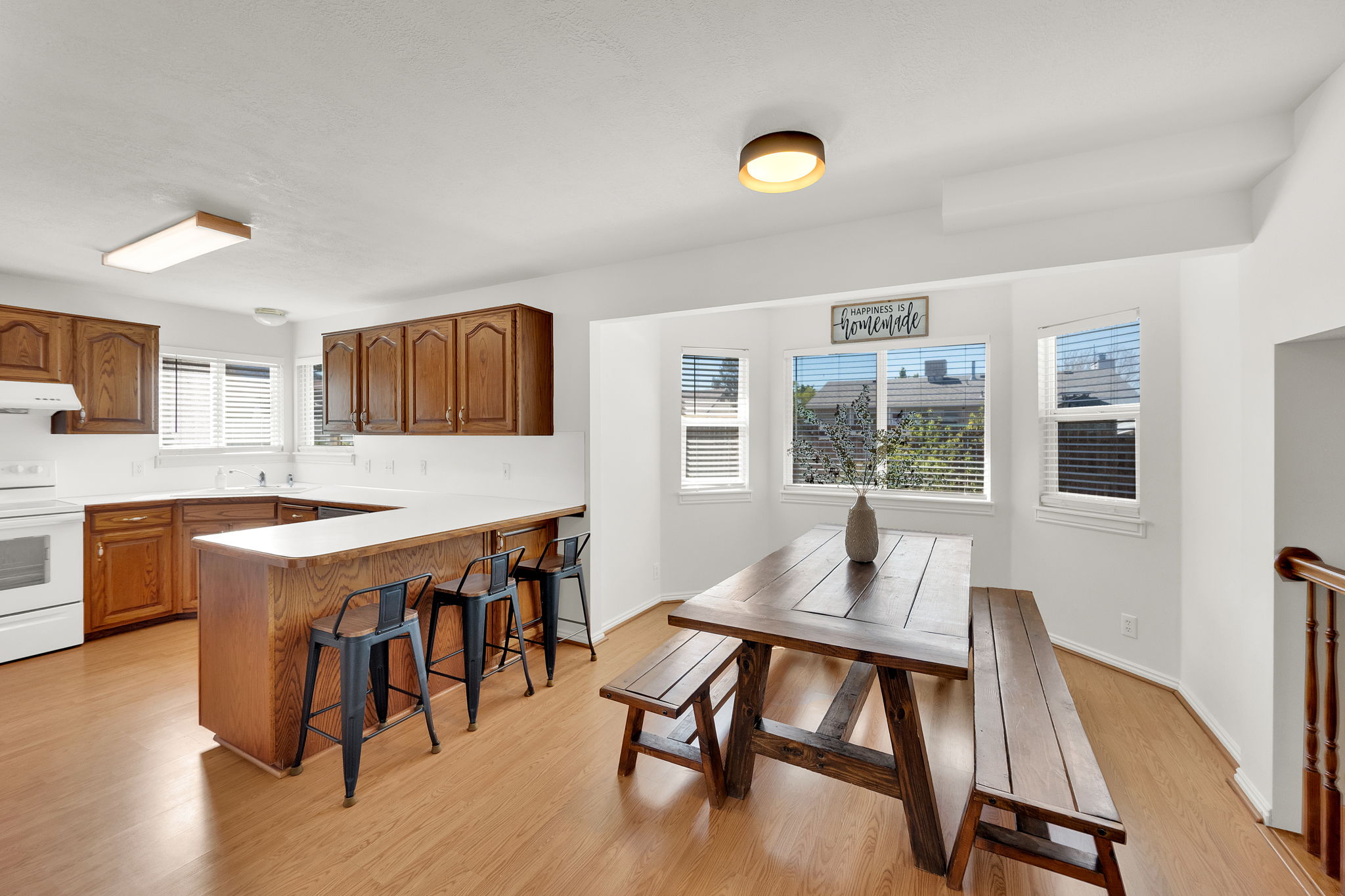 Kitchen and dining area featuring wood-finish flooring, wood cabinetry, white countertops, a U-shaped breakfast bar, and multiple windows
